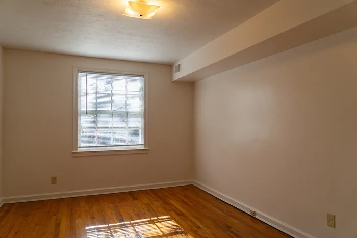 Bright and inviting empty room featuring polished hardwood flooring, a large window with charming views, and soft lighting.