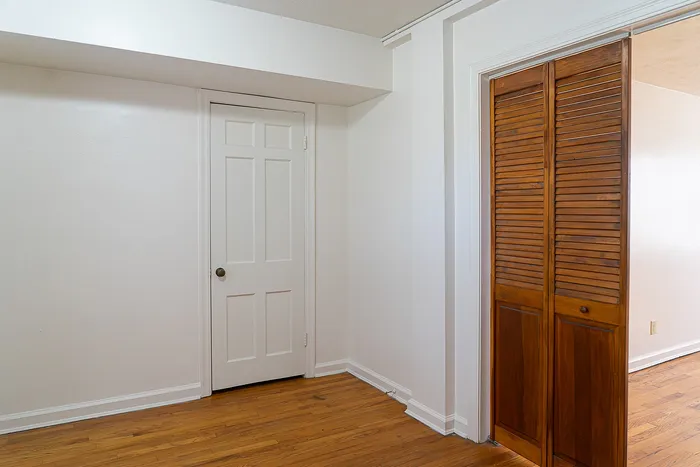 Bright room showcasing elegant hardwood floors, a sleek white door, and charming wooden closet doors, offering a modern and inviting space.