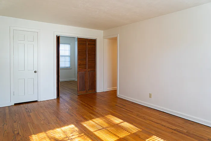 Bright and inviting room with polished wooden floors, fresh white walls, and warm natural light streaming through the window.