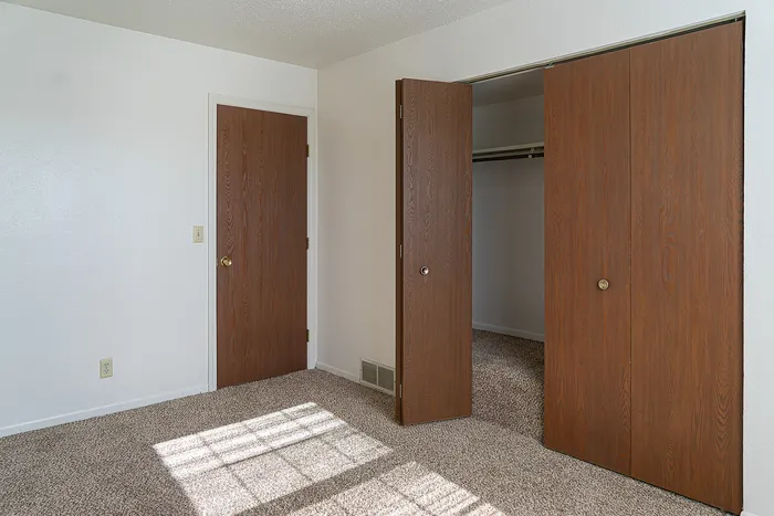 Bright room featuring rich wooden closet doors and a warm carpeted floor, perfect for a cozy, inviting bedroom space.