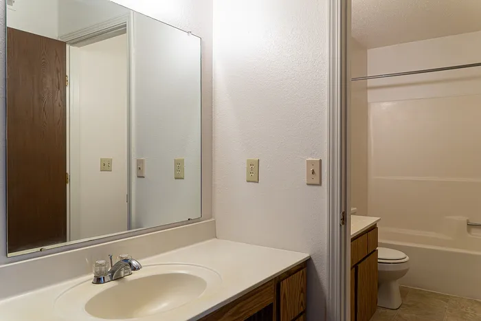 Bright and inviting bathroom featuring a large mirror, sleek white countertop, and modern fixtures, perfect for a refreshing start to your day.