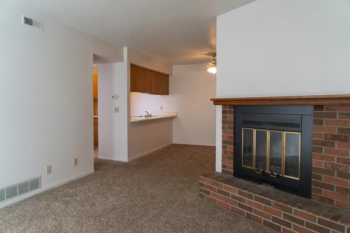Cozy living area featuring a charming brick fireplace and inviting carpet flooring, leading into a bright kitchen with wood accents.