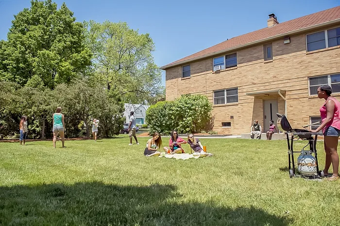 Vibrant outdoor scene of a spacious apartment complex lawn with people enjoying a picnic, barbecue, and games under clear blue skies.