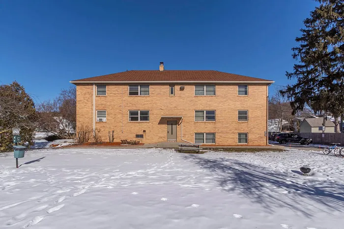Charming brick apartment building with a winter landscape, set against a clear blue sky offering tranquil suburban living.