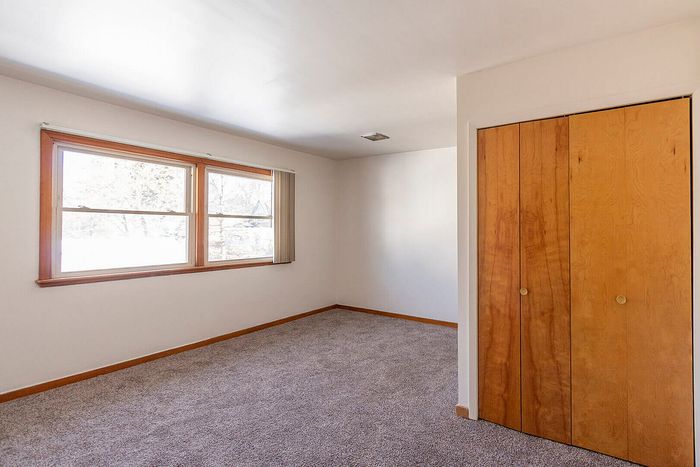Bright, inviting bedroom with large window, plush carpet, and wooden closet doors, perfect for a cozy retreat.