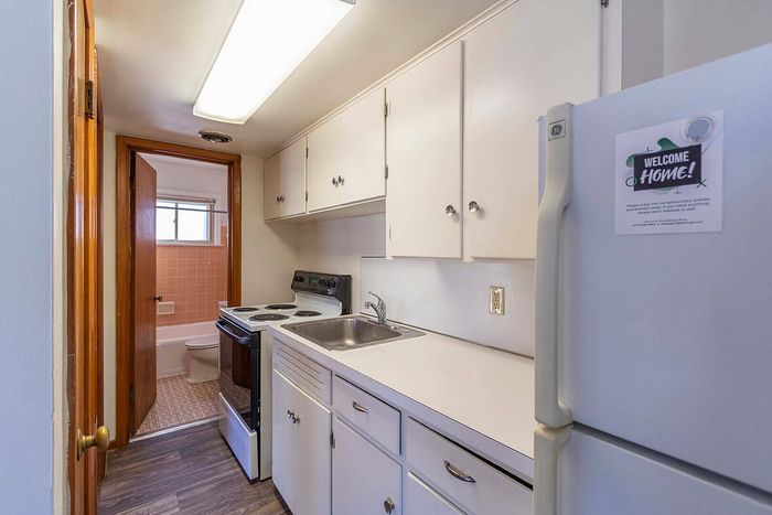 Charming compact kitchen with bright cabinetry, modern appliances, and a cozy aesthetic leading to a well-lit bathroom.