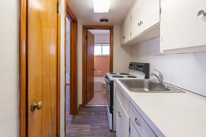 Compact and efficient kitchen design with clean white cabinetry, modern appliances, and a sleek countertop leading to a cozy bathroom.