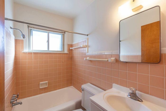 Charming retro bathroom with peach tiles, a large mirror, and natural light from a generous window.