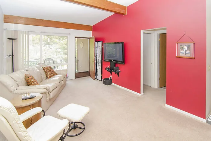 Inviting living room with vibrant red accent wall, elegant beige sofa, and large window offering serene forest views.