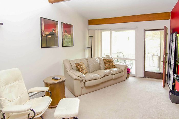 Bright and inviting living room with modern decor featuring a plush leather sofa, elegant white armchair, and wall art, leading to a sunny balcony.