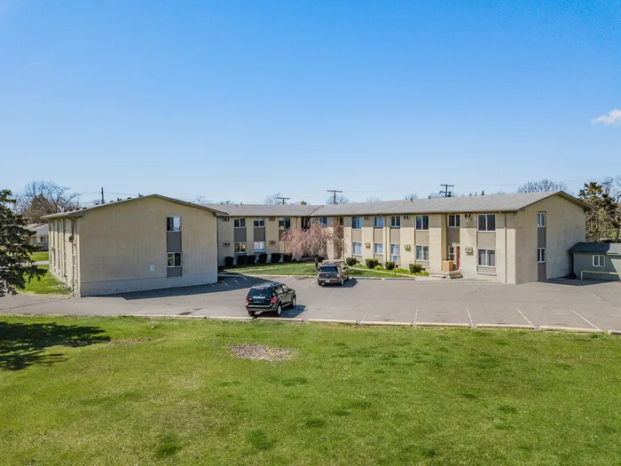 Charming two-story apartment complex surrounded by lush green lawns, featuring ample parking space and a peaceful suburban setting.