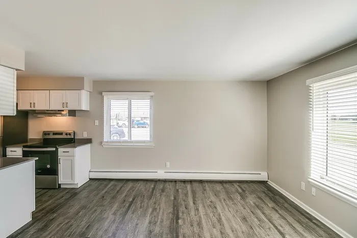 Bright and spacious living area with modern kitchen featuring sleek cabinetry, large windows, and elegant wood flooring.