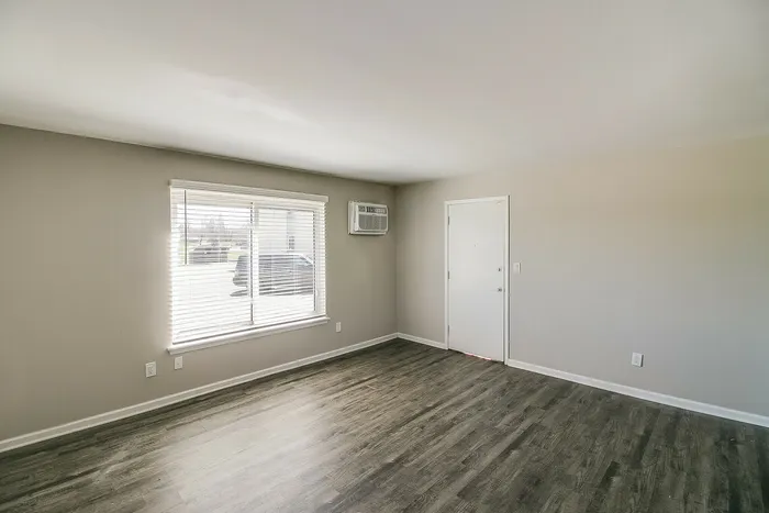 Bright and inviting living room with large window, sleek wood flooring, and a modern air conditioning unit.