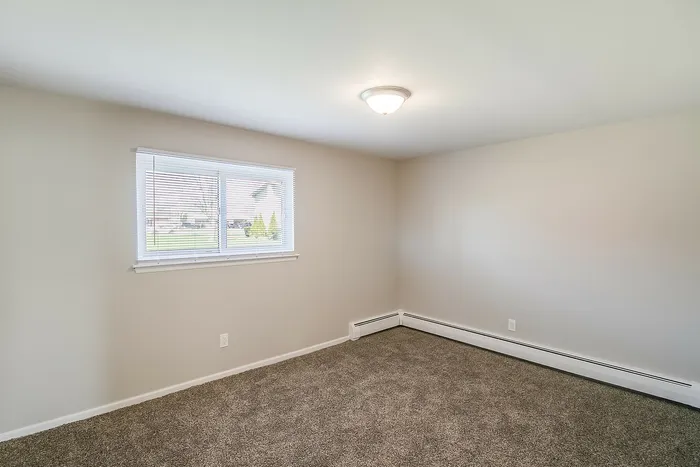Bright and inviting room featuring plush carpeting and a large window filling the space with natural light.