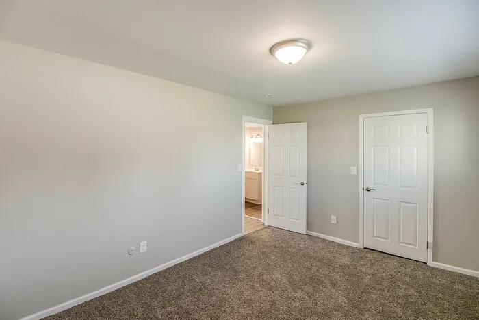Bright bedroom with plush carpet, stylish lighting, and an inviting ensuite bathroom.