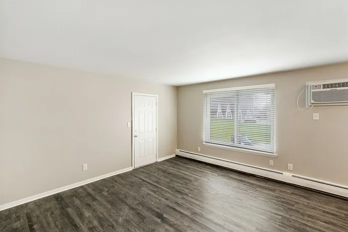 Bright and welcoming living space with modern wood flooring, large window, and sleek air conditioning unit, ideal for comfort and style.