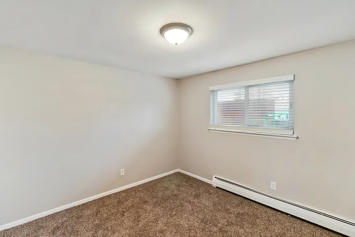 Bright and cozy room featuring plush carpet, large window with blinds, and stylish overhead lighting.