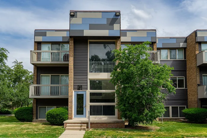 Modern apartment building with stylish geometric facade and private balconies, surrounded by lush greenery and sunny skies.