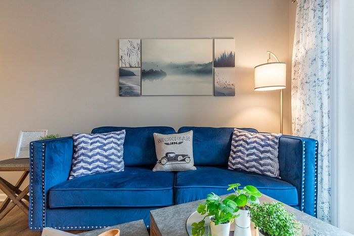 Inviting living room featuring a plush blue couch with patterned cushions, elegant artwork, and ambient lighting. Ideal for relaxation and style.