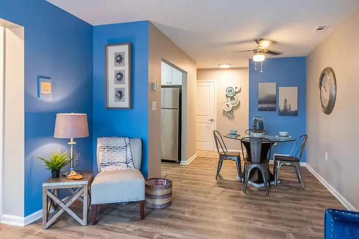 Inviting living area with modern blue accent walls, stylish decor, and a cozy reading nook, leading to a chic dining space with sleek metal chairs and a contemporary glass table.