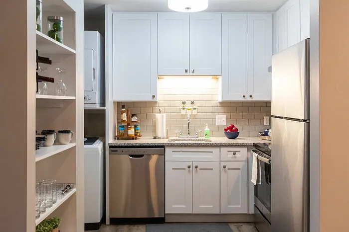 Chic modern kitchen with sleek white cabinets, stainless steel appliances, and elegant shelving for showcasing glassware and wine.