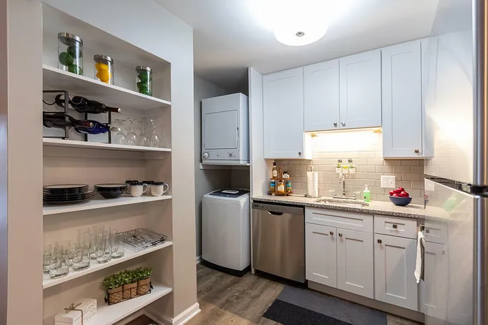 Modern kitchenette with sleek white cabinets, stainless steel appliances, and built-in shelving for stylish storage solutions.