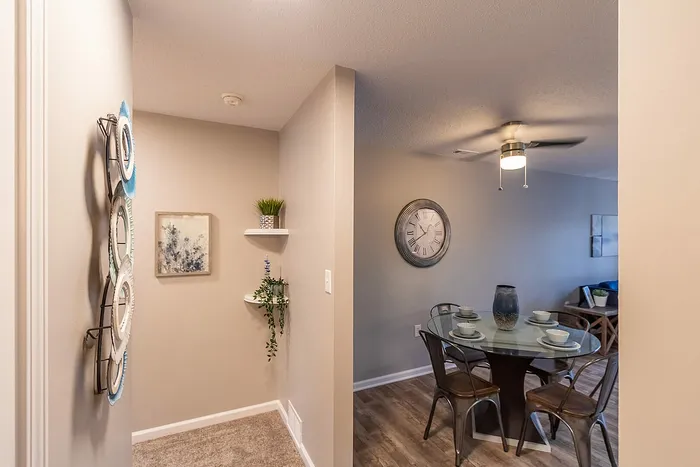 Charming dining area with a modern glass table set for four, accented by a stylish wall clock and elegant decor shelves, perfect for intimate gatherings.