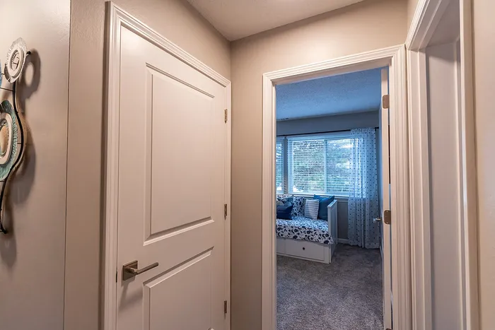 Inviting hallway leading to a cozy bedroom with large windows and plush carpeting.