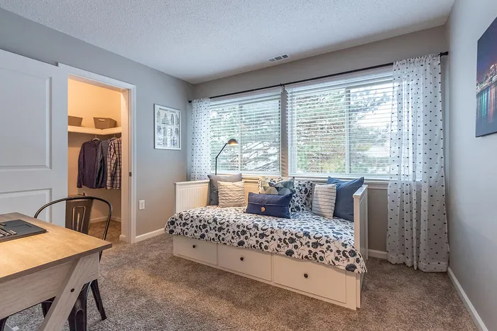 Cozy bedroom featuring a stylish daybed with patterned bedding, plush carpet, and a vibrant reading nook under large windows providing natural light.