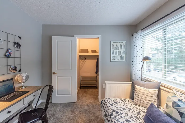 Cozy bedroom with a stylish workspace, featuring a modern desk, comfortable seating, and ample natural light from large windows.
