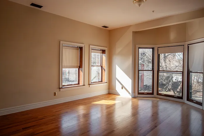 Bright and inviting living space with large bay windows offering scenic views, featuring elegant hardwood floors and ample natural light.
