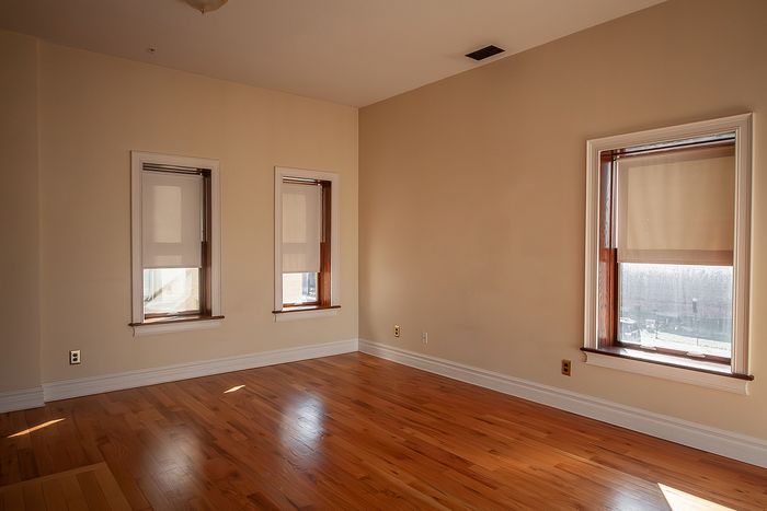 Bright and airy empty room with warm hardwood floors and three large windows, perfect for a cozy living space.