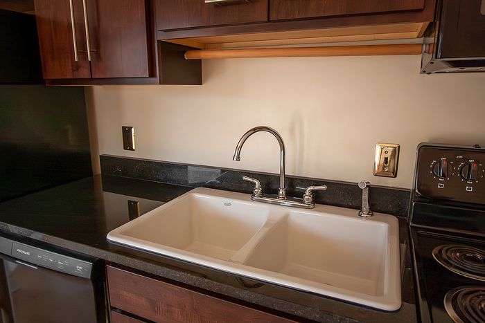 Modern kitchen with sleek dark wood cabinetry, double sink, and glossy black countertops.