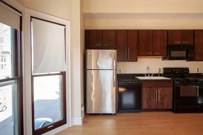 Sleek modern kitchen with stainless steel appliances, rich wooden cabinetry, and sunlit windows.