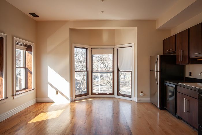 Bright living space with elegant bay windows and sleek kitchen featuring modern appliances and warm hardwood flooring.