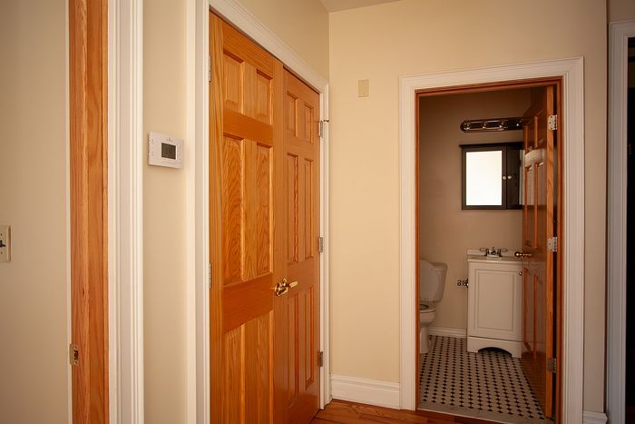 Inviting apartment hallway with warm wooden doors leading to a cozy bathroom featuring classic checkered tile flooring.