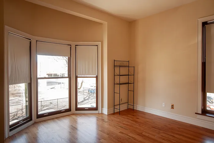 Bright apartment room with large bay windows and elegant wooden flooring, offering abundant natural light and a cozy atmosphere.