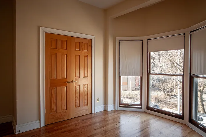 Bright apartment interior with elegant hardwood floors, large wooden doors, and expansive bay windows offering serene views.