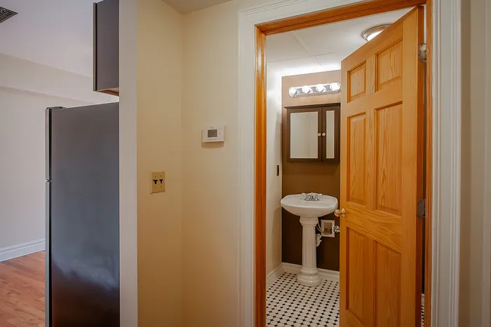 Charming bathroom entrance with elegant wooden door, stylish pedestal sink, and chic checkered floor tiles.