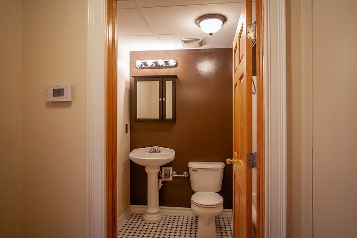 Charming bathroom with elegant pedestal sink, modern lighting, and classic black-and-white tiled floor.
