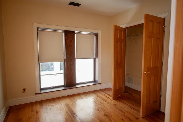 Cozy room with elegant wooden flooring, a large window for abundant natural light, and a spacious closet with wooden doors.