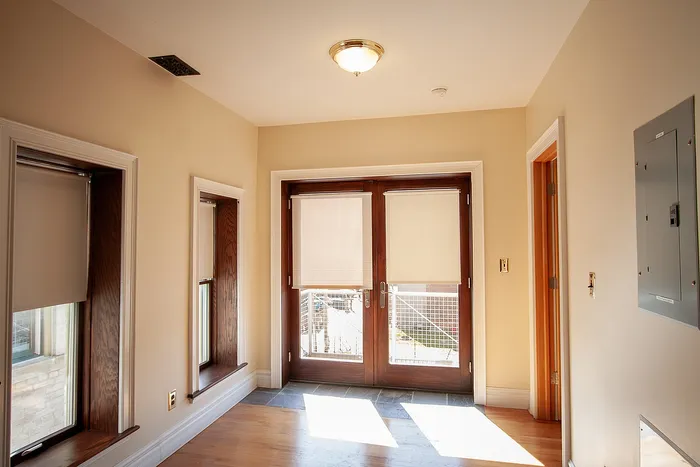 Bright apartment entryway featuring wooden French doors, warm natural lighting, and sleek hardwood floors, creating an inviting atmosphere.