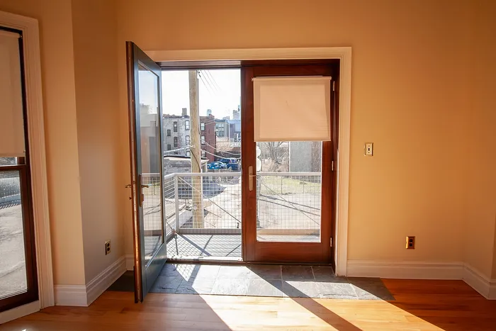 Bright apartment entryway with elegant wooden door opening to a sunny balcony and scenic city views.