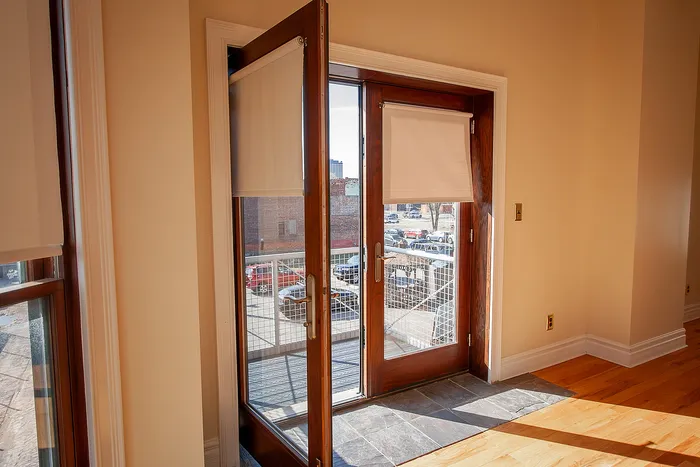 Bright, inviting room with elegant glass doors leading to a sunlit balcony, featuring warm wood accents and sleek stone flooring.