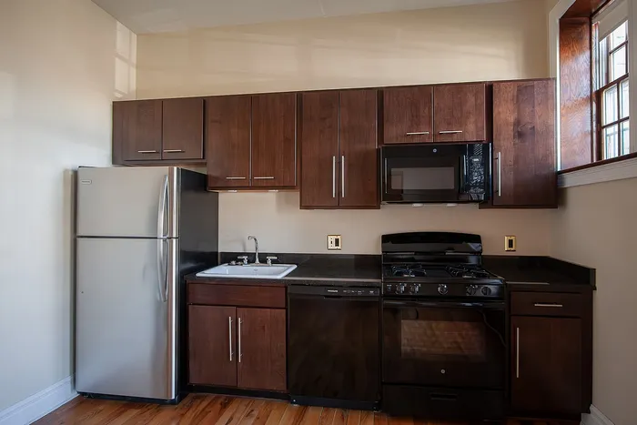 Modern apartment kitchen with sleek appliances, rich wooden cabinets, and large windows for natural light.