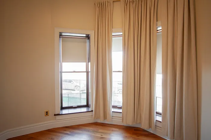 Bright room with elegant tall windows, chic beige curtains, and warm hardwood flooring.
