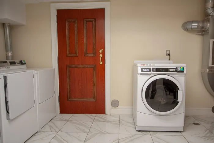 Inviting laundry room with sleek modern appliances, elegant red door, and pristine marble flooring.