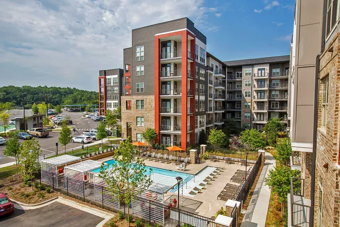 Modern apartment complex featuring a stylish pool area, lush greenery, and ample parking, set in a vibrant urban environment.