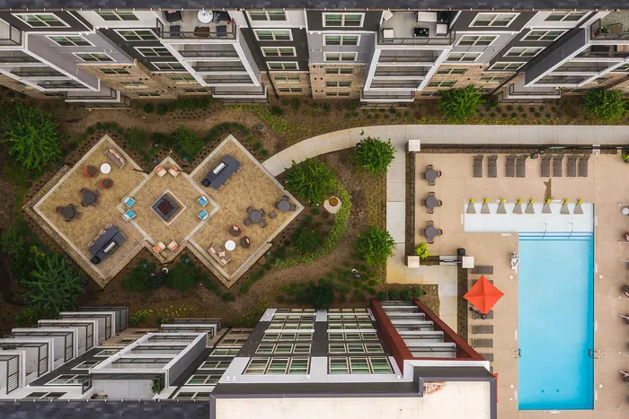 Aerial view of luxurious apartment complex featuring a stylish courtyard with seating areas, lush greenery, and a sparkling swimming pool with poolside lounges.