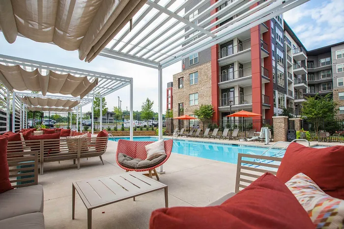 Luxurious apartment complex with a stylish poolside lounge featuring plush seating and shaded pergolas, perfect for relaxation.